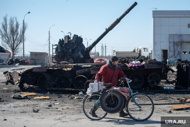 Мужчина в Мариуполе катит велосипед на фоне сгоревшего танка
