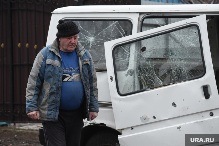 Местный житель на фоне поврежденного обстрелом своего автомобиля