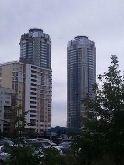 На фоне двух высотных зданий идущий по канату человек кажется маленькой точкой