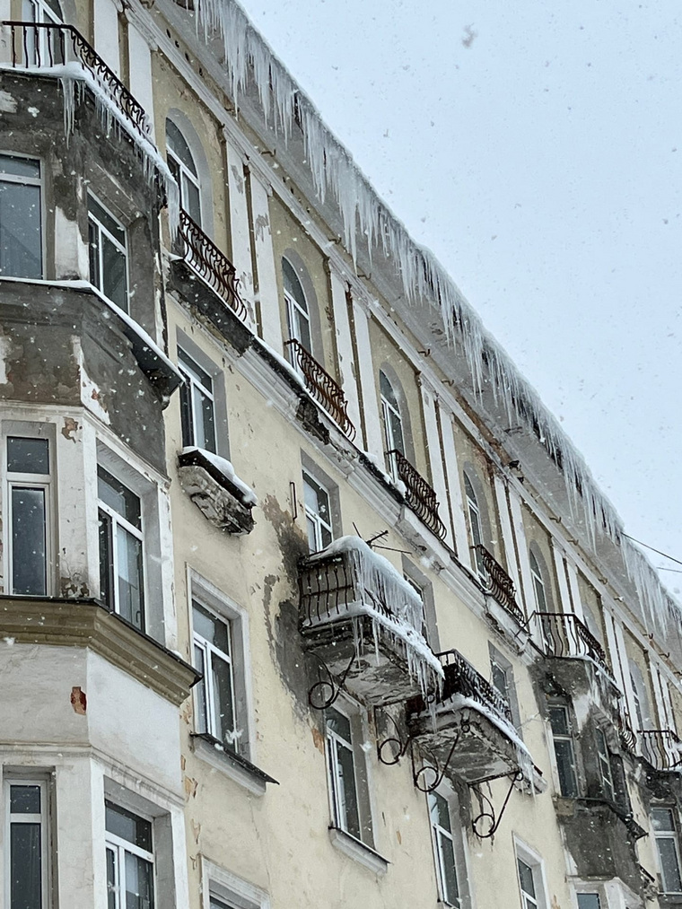 С крыши дома, откуда упал снег, угрожающе свисают сосульки